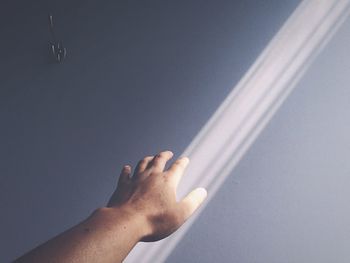 Cropped image of person touching sunlight falling on wall