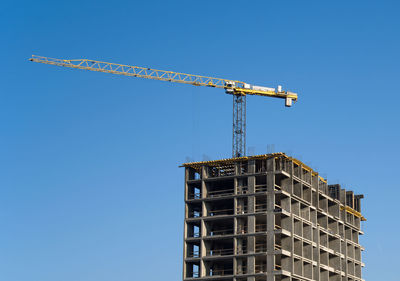 Low angle view of crane on building against clear blue sky