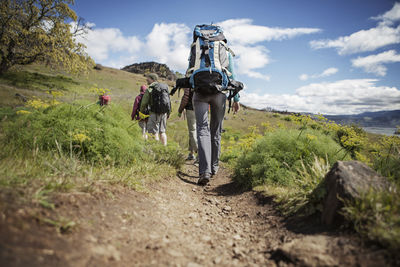 Rear view of hikers carrying backpack while walking on hill