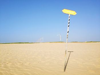 Information sign on beach against clear blue sky
