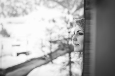 Smiling woman looking through window during winter