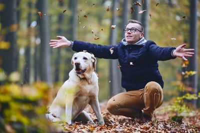 Man throwing autumn leaves on dog in forest