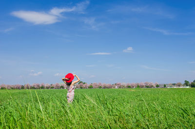 Woman standing amidst plants on field against sky during sunny day