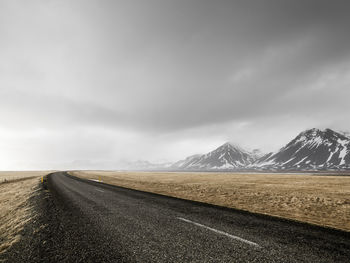 Empty road leading towards mountains against sky
