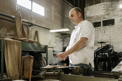 Low angle side view of concentrated male woodworker creating wooden details while standing in grungy garage at daytime