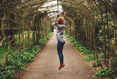 Woman jumping on footpath covered with plants at park