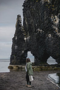 Rear view of woman standing on rock by sea