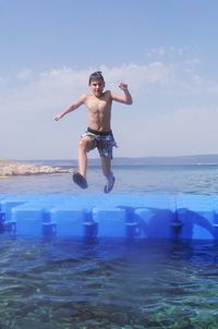 Full length of shirtless boy jumping in sea against sky