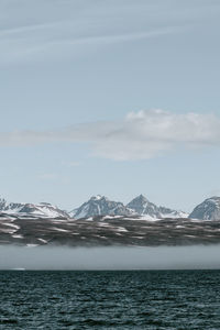 Scenic view of sea by snowcapped mountains against sky