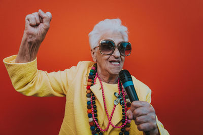 Portrait of senior woman singing on microphone against red background