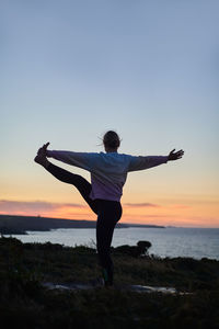 Rear view of woman doing yoga against sky during sunset