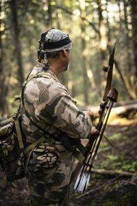 Hunter holding bow and arrow while standing in forest