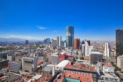 Aerial view of buildings in city against blue sky