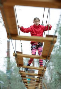 Low angle view of girl standing on rope bridge against sky