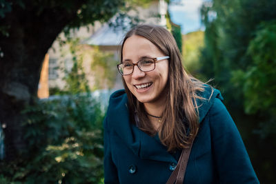 Smiling woman looking away while standing against trees