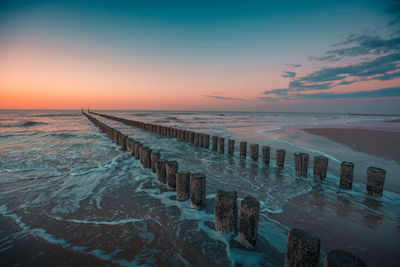 Wooden posts in sea against sky during sunset