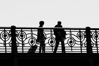 Silhouette men on railing against clear sky