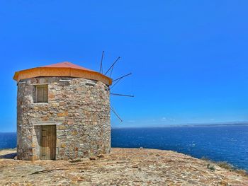 Lighthouse by sea against clear blue sky