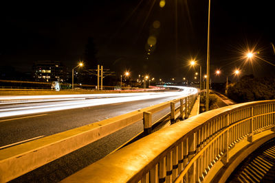 Light trails on snow covered bridge against sky at night