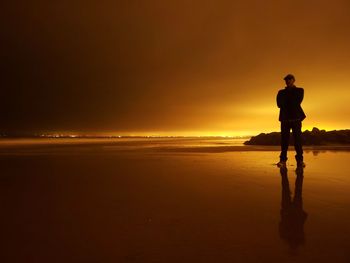 Full length of man standing at beach against sky during sunset