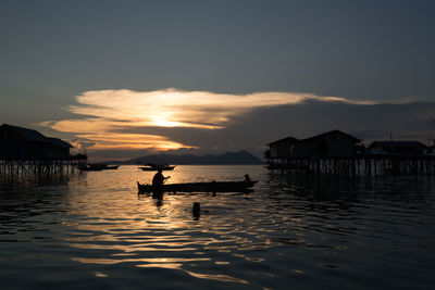 Silhouette man in boat on sea against cloudy sky during sunset