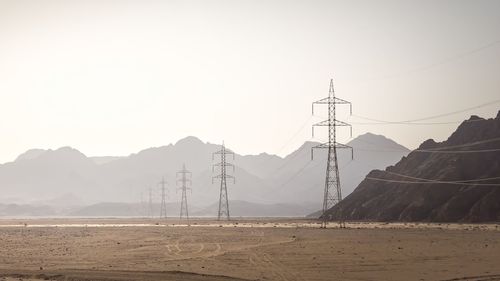 Electricity pylons on landscape against clear sky