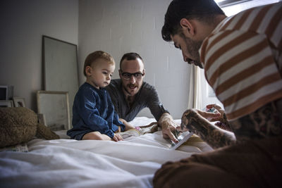 Fathers showing tablet computer to daughter while sitting on bed at home