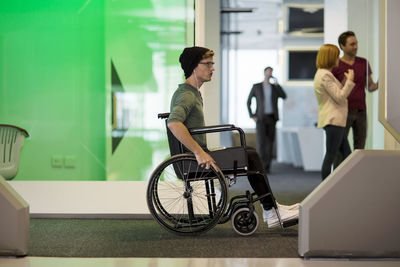 Young man in wheelchair listening to music in office