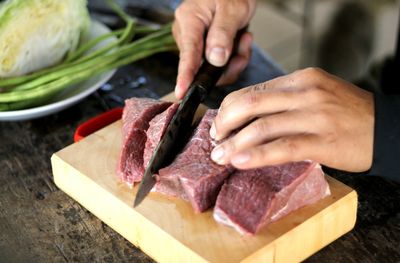 Cropped image of chef cutting meat at kitchen counter