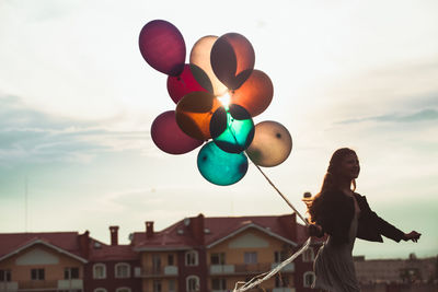 Low angle view of woman holding colorful balloons against building