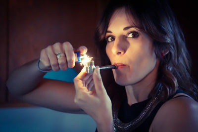 Close-up portrait of beautiful woman burning pipe against wall
