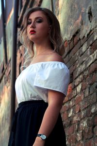 Low angle portrait of woman standing by weathered brick wall