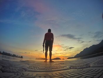 Rear view of man standing on pier against sky during sunset