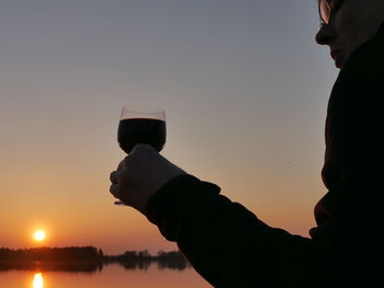 Close-up of man holding beer glass against clear sky during sunset