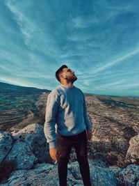 Young man standing on rock against sky