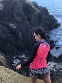 Rear view of young woman standing on cliff sea