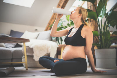 Young happy and cheerful beautiful pregnant woman taking a break, hydrating, drinking water from the