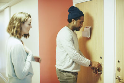 Woman looking at male friend opening door lock in college dorm