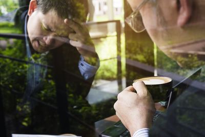 Frustrated businessman holding coffee cup reflecting on window in office