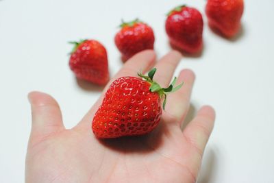 Close-up of hand holding strawberry over white background