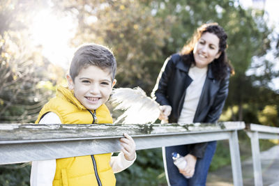 Mother tickling son with feather by railing in park