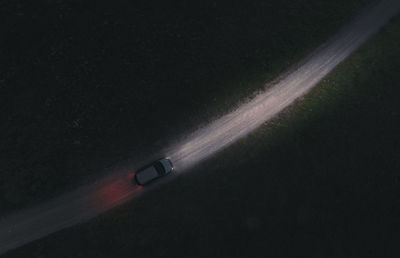 The car moves on a dirt road at night. the road is lit with headlights. theme of road transport