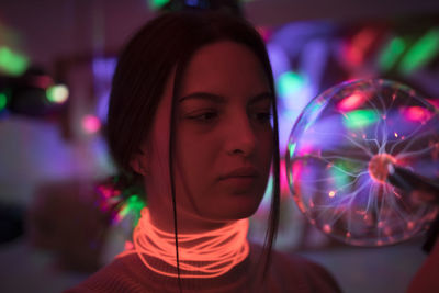 Close-up of woman wearing illuminated necklace holding lighting equipment in room