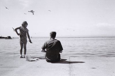 Rear view of father and daughter at beach against sky