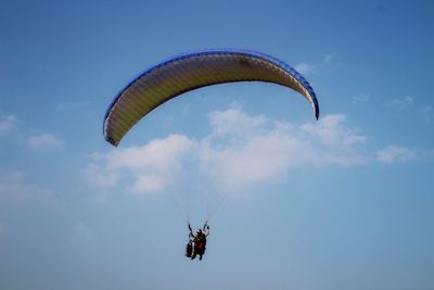 Low angle view of people paragliding against sky