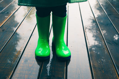 Low section of person wearing rubber boots while standing on wet boardwalk