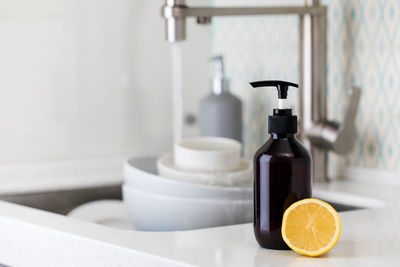 Bottle with eco friendly dishwashing detergent with lemon on the background of a sink 