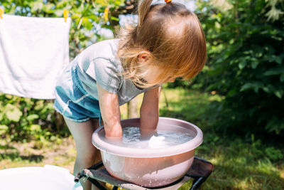 Little preschool girl helps with laundry. child washes clothes in garden