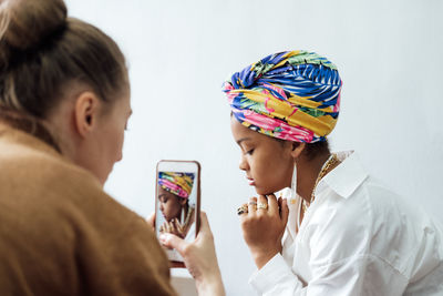 Fashion designer taking photo of young african woman model with colorful shawl on her head and