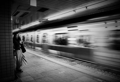 Woman by blurred motion of train at railroad station platform